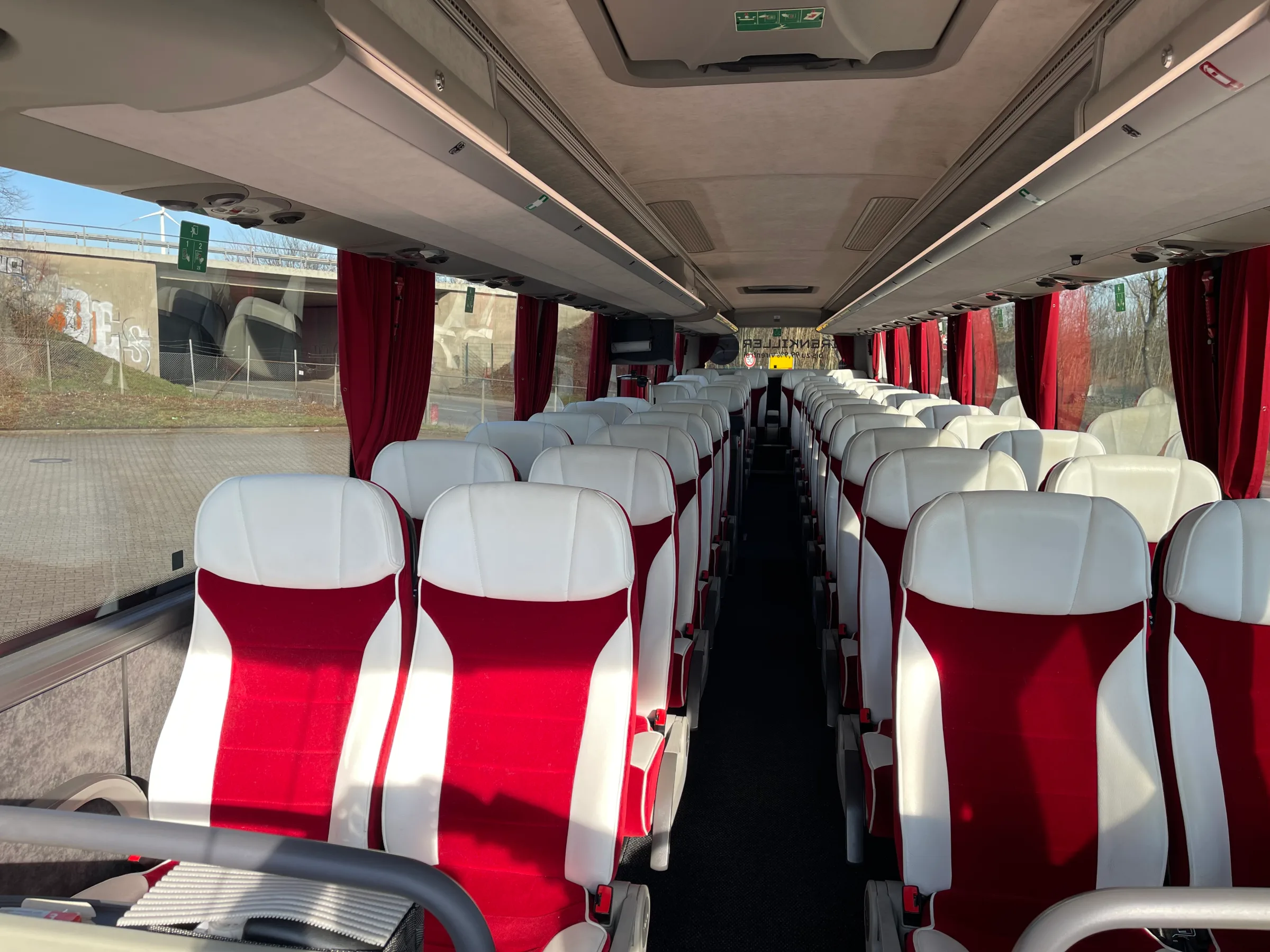 Blick durch den Mittelgang eines modernen Reisebusses mit rot-weißen Polstersitzen und roten Vorhängen