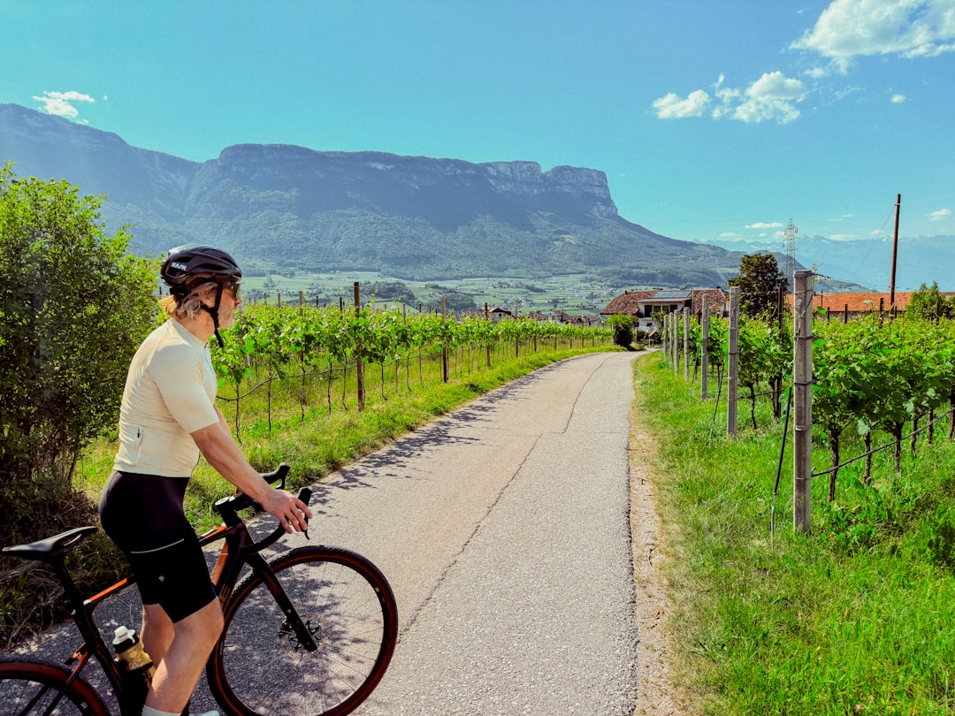 Rennradfahrer auf einem asphaltierten Weg durch Südtiroler Weinberge mit Blick auf markante Bergmassive unter blauem Himmel