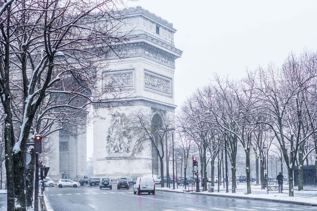 Verschneiter Triumphbogen in Paris mit kahlen, weißen Bäumen und fahrenden Autos bei winterlichem Wetter