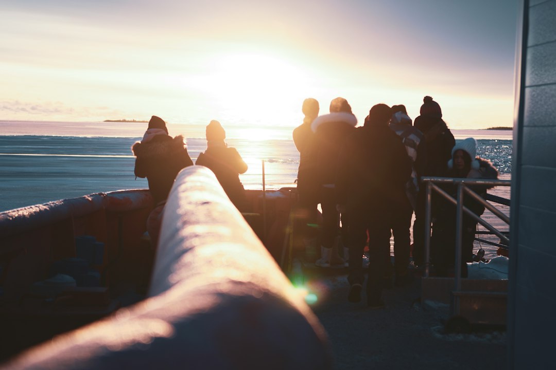 Reisegruppe in Winterkleidung an Deck eines Schiffes blickt bei Sonnenuntergang auf eine weite Eislandschaft