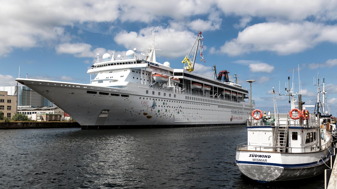 Großes weißes Kreuzfahrtschiff Star Libra neben einem kleineren Boot im Hafen von Wismar unter blauem Himmel mit Wolken