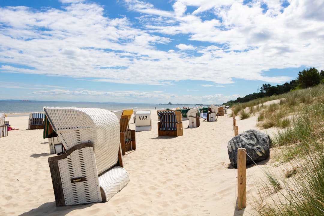 Weiße Strandkörbe an einem sonnigen Sandstrand der Ostsee vor bewachsenen Dünen unter blauem Himmel mit Schönwetterwolken