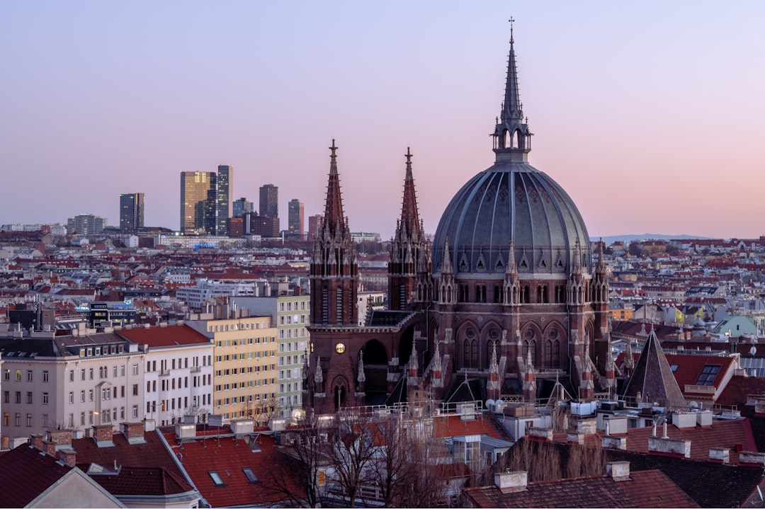 Blick über die Dächer von Wien auf die beleuchtete Kirche Maria vom Siege und die Skyline bei dämmerndem Abendhimmel